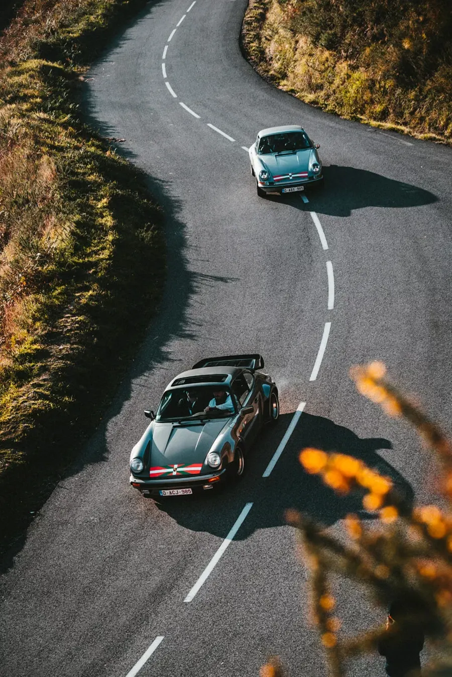 Vue aérienne de deux Porsche 911 classiques sur une route de montagne sinueuse lors d'un rallye