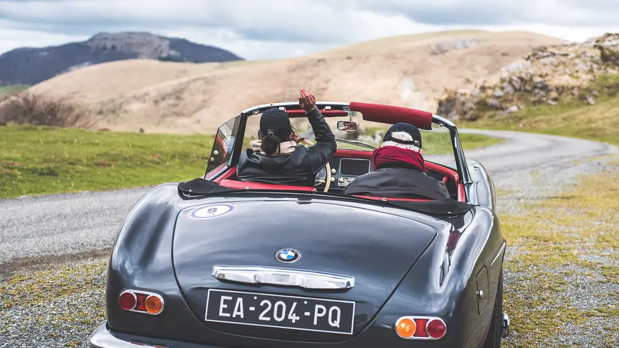 Passagère saluant depuis une BMW 503 cabriolet vintage traversant la campagne