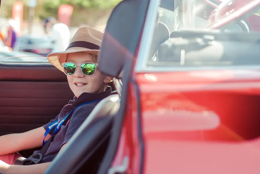 Jeune garçon souriant avec des lunettes de soleil dans un cabriolet vintage lors d'un événement automobile